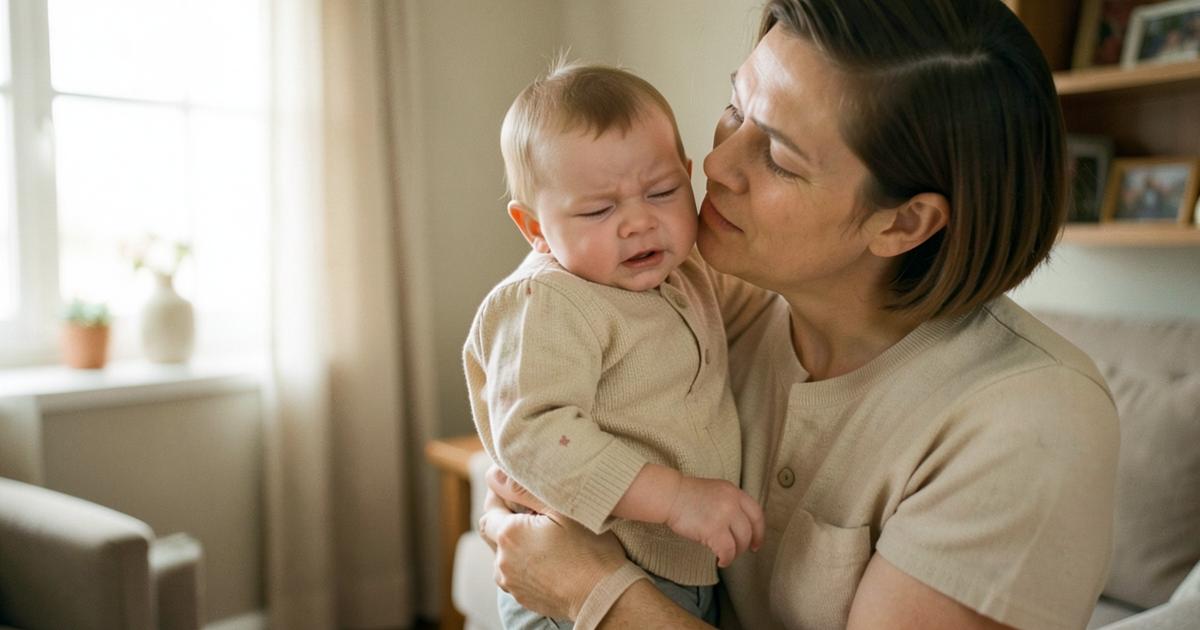 Mamá consolando a su bebé que llora, sosteniéndolo contra el hombro en una sala con luz suave