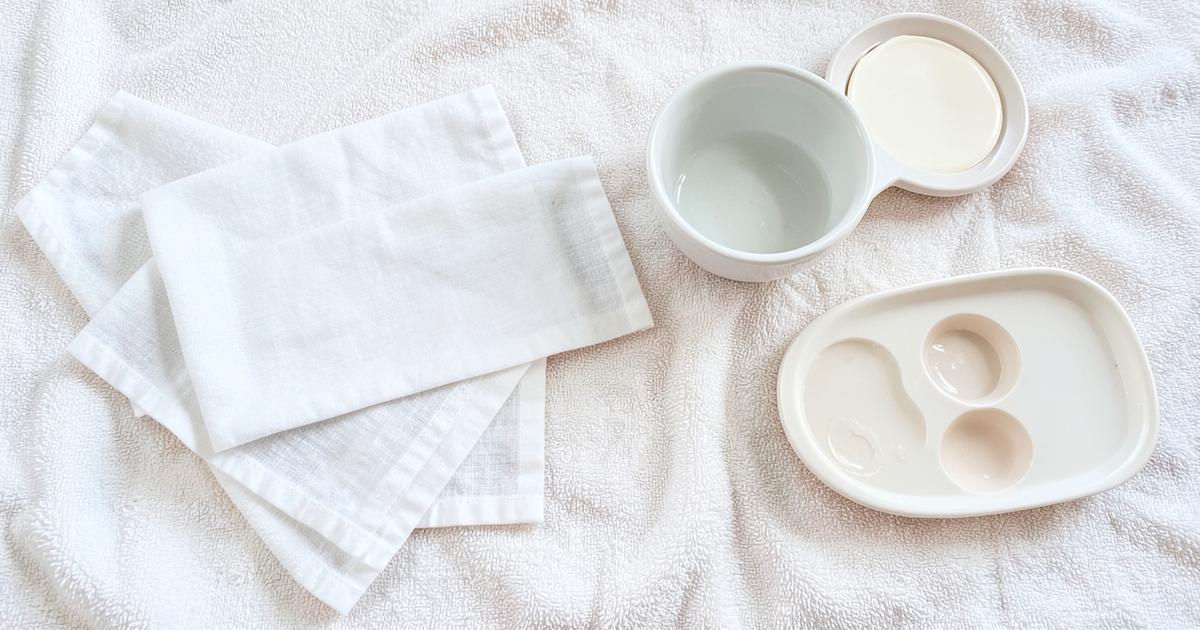 Gasas de algodón, un paño de muselina doblado y un recipiente con agua sobre una toalla blanca